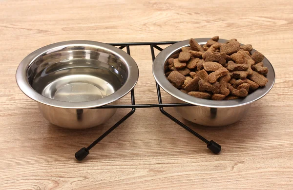 Comida de cão seco e água em tigelas de metal em fundo de madeira — Fotografia de Stock
