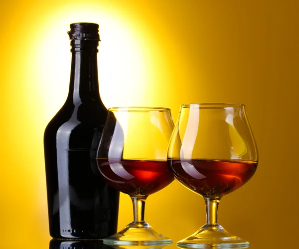 Okulary z brandy i butelka na żółtym tle — Zdjęcie stockowe