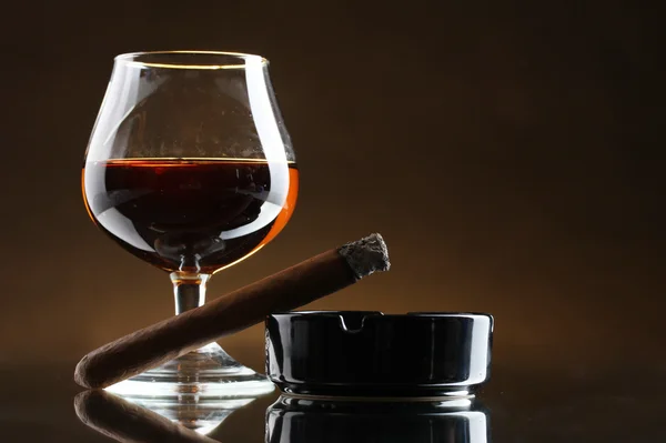 Glas cognac en een sigaar op bruine achtergrond — Stockfoto