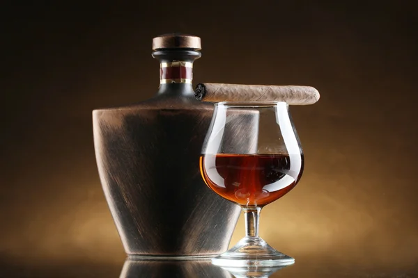 Butelkę i kieliszek brandy i cygaro na brązowym tle — Zdjęcie stockowe