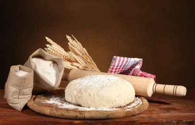 Dough and bags with flour on wooden table on brown background clipart