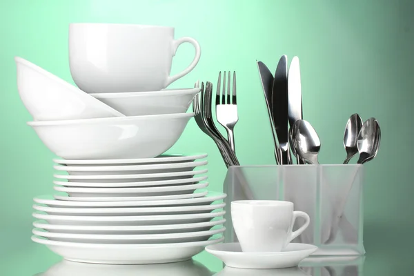 Čisté talíře, šálky a příbory na zeleném pozadí — Stock fotografie