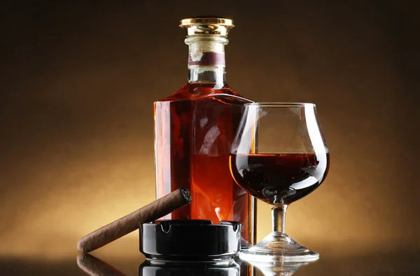 Láhve a sklenky brandy a doutník na hnědé pozadí — Stock fotografie