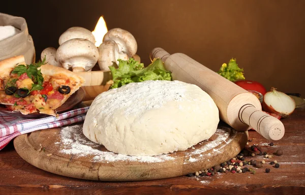 Leckerer Pizzateig, Gewürze und Gemüse auf Holztisch auf braunem Hintergrund — Stockfoto