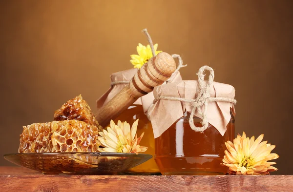 Dos frascos de miel, panales y rociadores de madera sobre la mesa sobre fondo amarillo —  Fotos de Stock