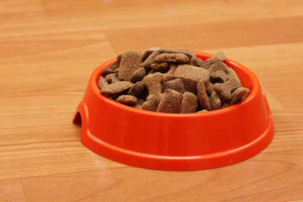 Cibo secco per cani in una ciotola arancione sul pavimento — Foto Stock