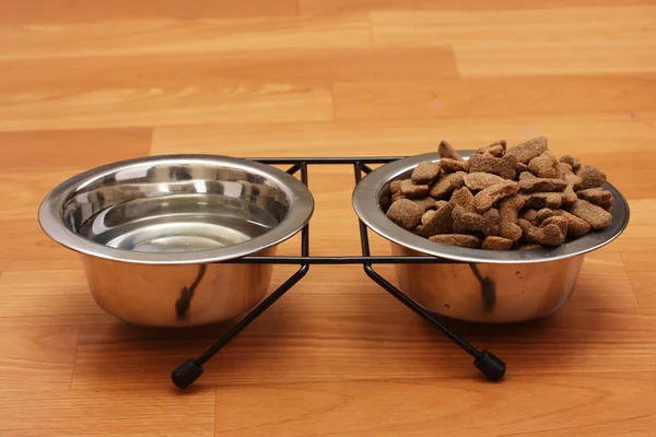 Dry dog food and water in metal bowls on the floor — Stock Photo, Image