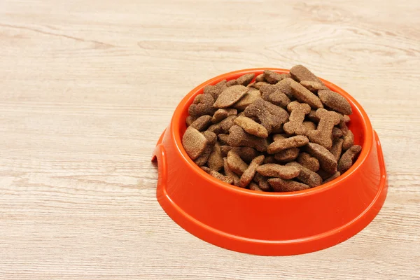 Comida seca para perros en un tazón naranja sobre fondo de madera — Foto de Stock