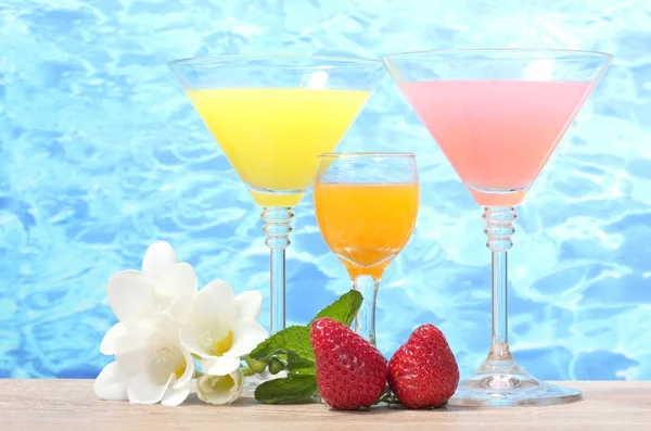 Exotic cocktails, strawberry and flowers on table on blue sea background — Stock Photo, Image