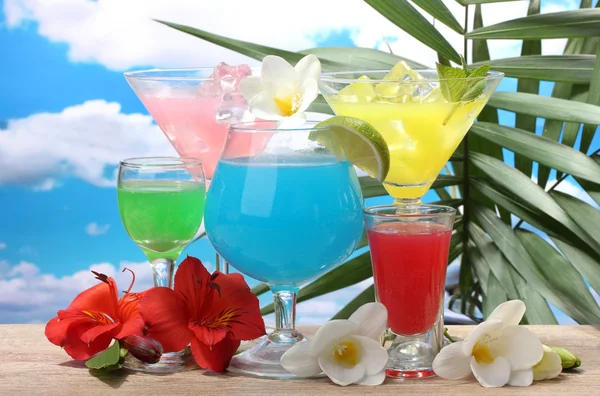 Exotic cocktails and flowers on table on blue sky background — Stock Photo, Image
