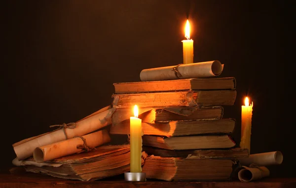 stock image Pile of old books with candle and scroll in dark