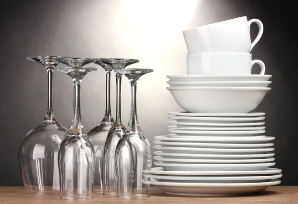 Ren tallrikar, glas och koppar på träbord på grå bakgrund — Stockfoto
