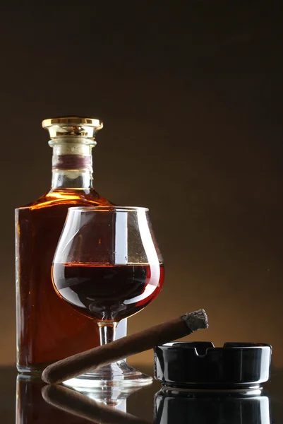 Fles en glas brandy en sigaar op bruine achtergrond — Stockfoto