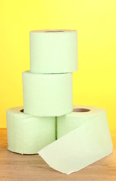 Green rolls of toilet paper on wooden table on yellow background — Stock Photo, Image