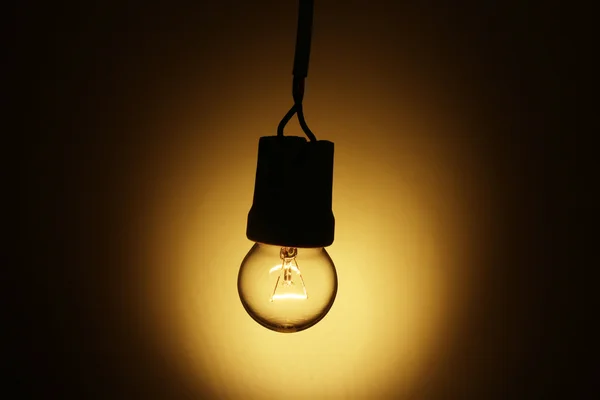 stock image A lit light bulb on yellow background