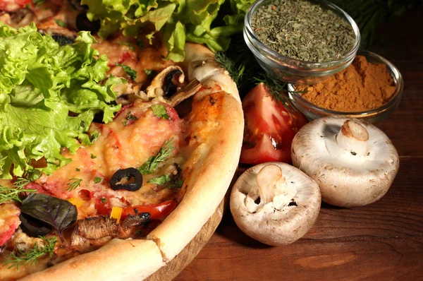 Pyszną pizzę, warzywa i przyprawy na drewnianym stole na brązowym tle — Zdjęcie stockowe