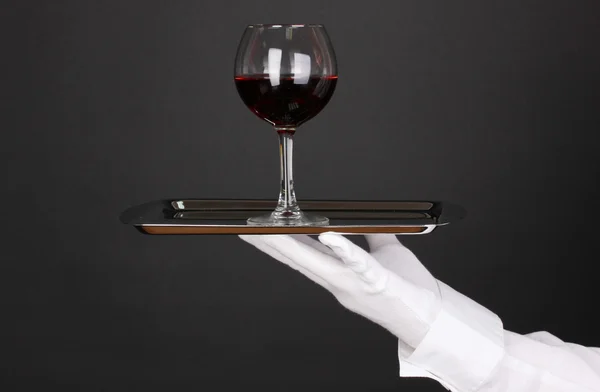 Hand in glove holding silver tray with wineglass isolated on black — Stock Photo, Image