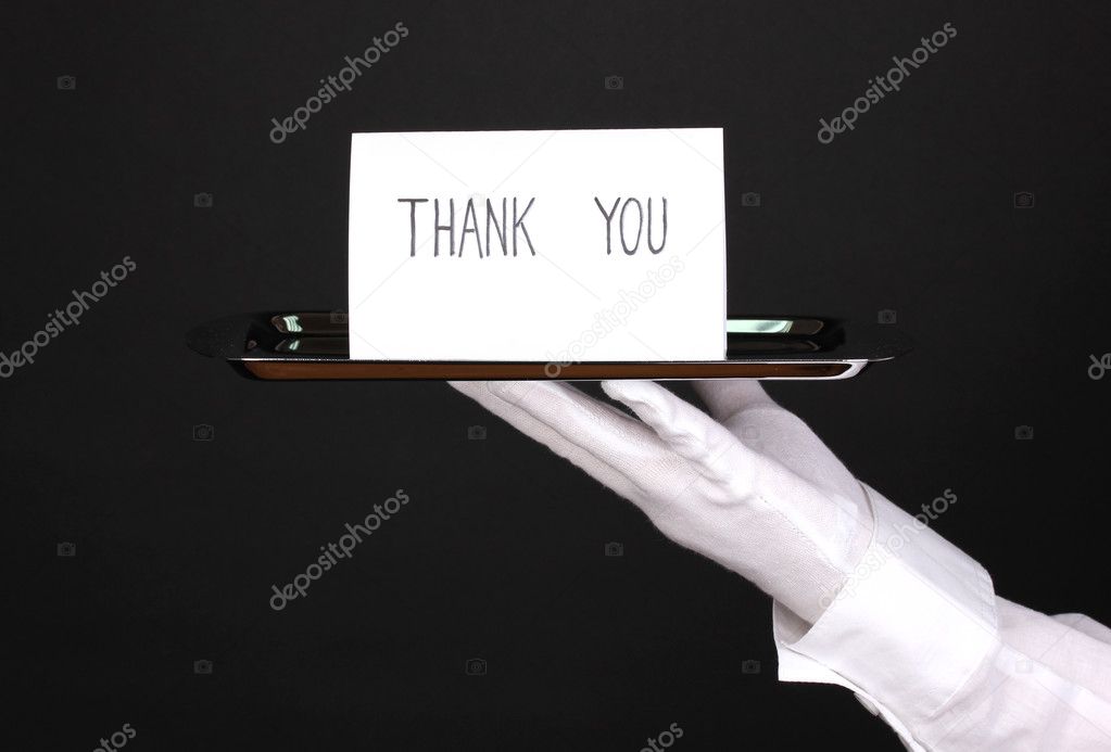 Hand in glove holding silver tray with card saying thank you isolated on black