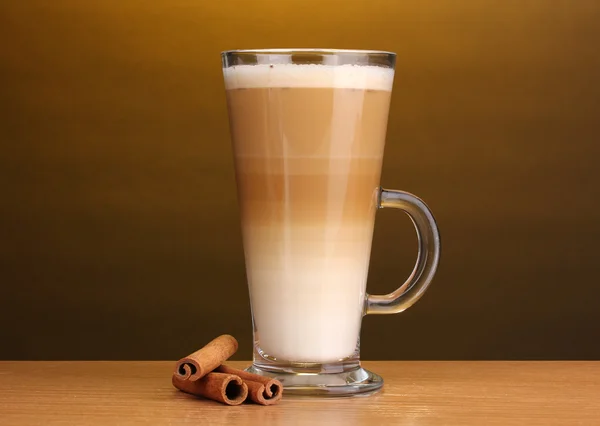 Latte parfumé dans une tasse en verre et cannelle sur table en bois sur fond marron — Photo