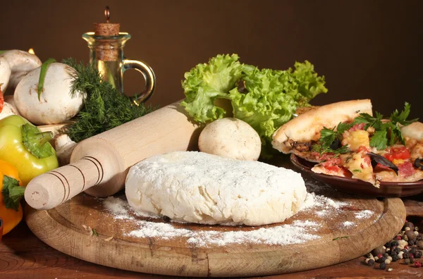 Delicious pizza dough, spices and vegetables on wooden table on brown background — Stock Photo, Image