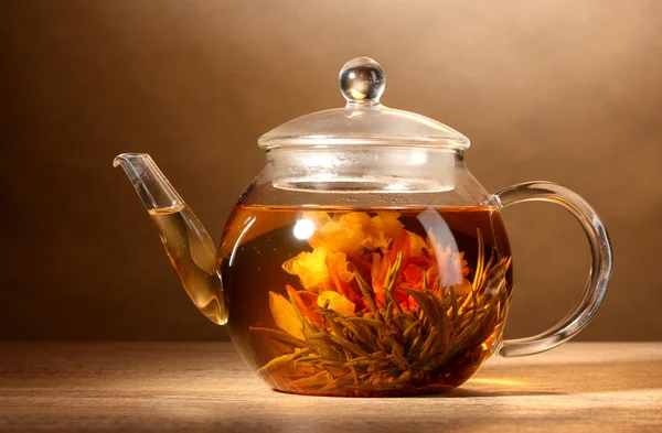 Стеклянный чайник с экзотическим зеленым чаем на деревянном столе на коричневом фоне — стоковое фото