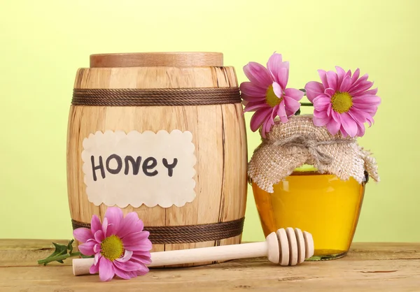 Miel dulce en barril y tarro con rociador sobre mesa de madera sobre fondo verde — Foto de Stock