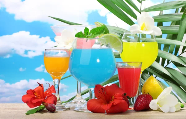 Exotic cocktails and flowers on table on blue sky background