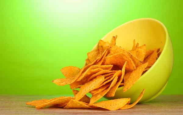 Smakelijke potato chips in groene kom op houten tafel op groene achtergrond — Stockfoto