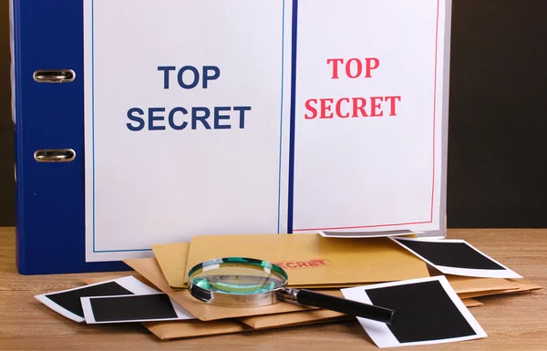 Envelopes e pastas com selo ultra-secreto e lupa com papéis fotográficos sobre mesa de madeira sobre fundo marrom — Fotografia de Stock