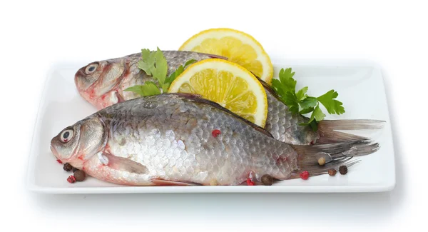 Świeże ryby z cytryną i natką pietruszki na płytkę na białym tle — Zdjęcie stockowe