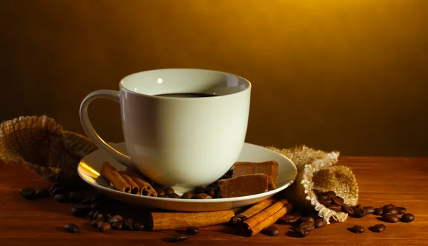 Чашка кофе и бобов, коричные палочки и шоколад на деревянном столе на коричневом фоне — стоковое фото