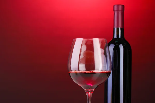 Fles van grote wijn en wijnglas op rode achtergrond — Stockfoto