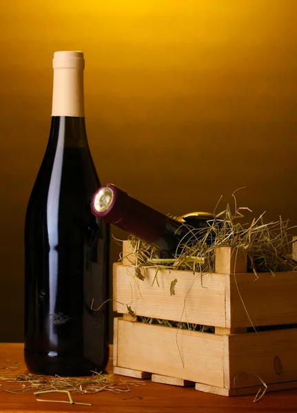 Láhev značkového vína v bedně na dřevěný stůl na hnědé pozadí — Stock fotografie