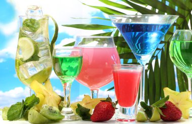 Glasses of cocktails on table on blue sky background clipart