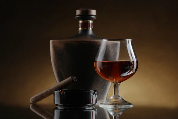 Botella y vaso de brandy y cigarro sobre fondo marrón —  Fotos de Stock