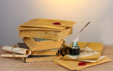 Old books, scrolls, feather pen and inkwell on wooden table on grey background clipart