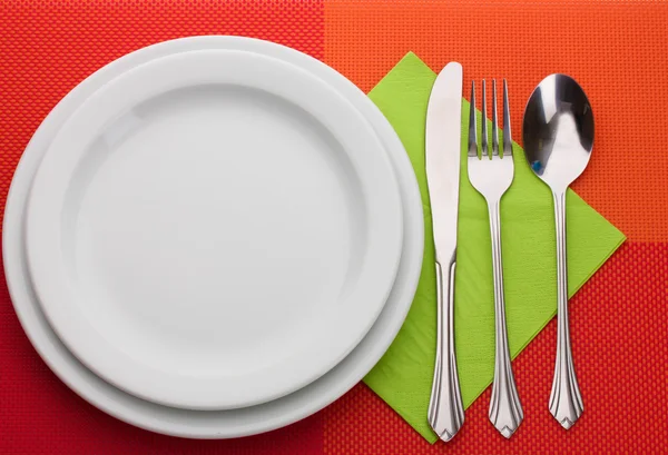 Белая пустая тарелка с вилкой, ложкой и ножом на красной скатерти — стоковое фото