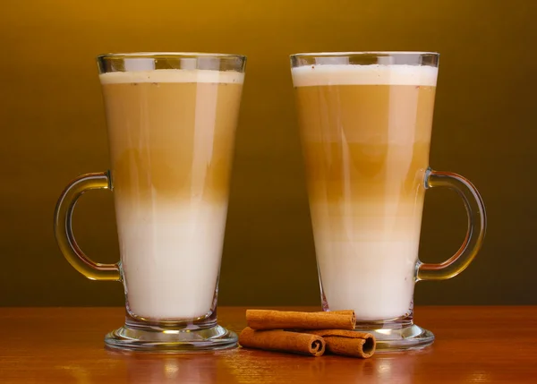 Fragante café con leche en copas de vidrio y canela sobre mesa de madera sobre fondo marrón — Foto de Stock
