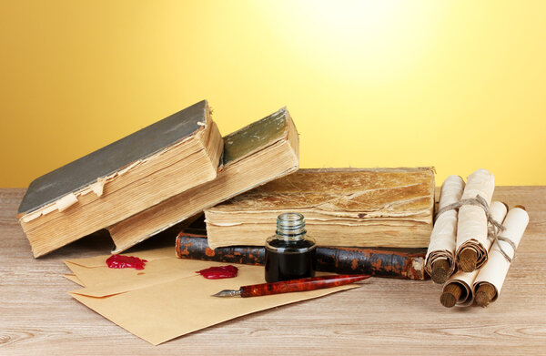 Old books, scrolls, ink pen and inkwell on wooden table on yellow background