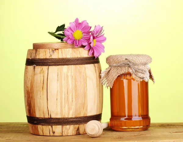 Süßer Honig in Glas und Fass mit Nieselregen auf Holztisch auf grünem Hintergrund — Stockfoto