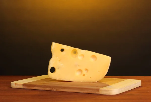 Stock image Cheese on cutting board on wooden table on brown background