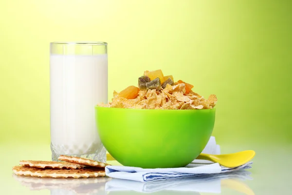 Smakelijke cornflakes in groene kom en glas melk op groene achtergrond — Stockfoto
