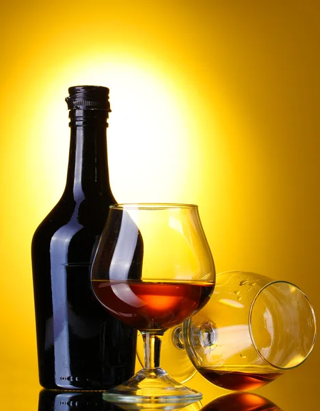 Glazen van brandy en fles op gele achtergrond — Stockfoto