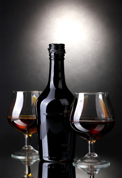 Lunettes de brandy et bouteille sur fond gris — Photo
