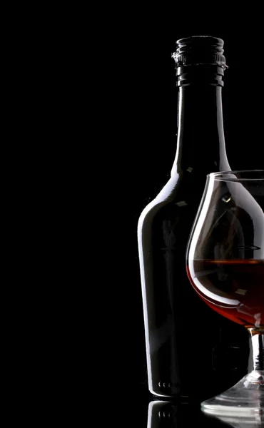 Vaso de brandy y botella sobre fondo negro —  Fotos de Stock