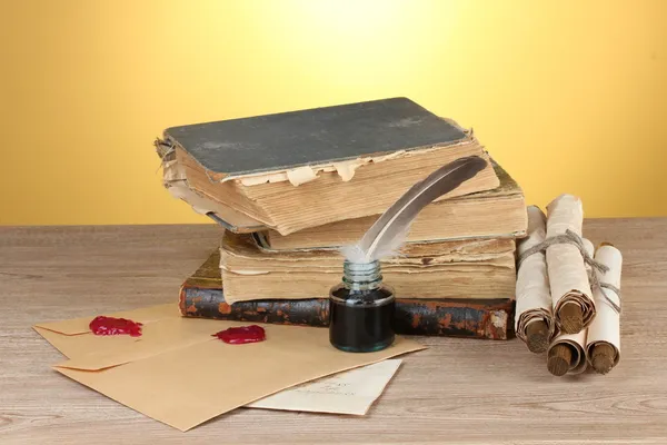 Libri antichi, pergamene, penna piuma e calamaio su tavolo di legno su sfondo giallo — Foto Stock