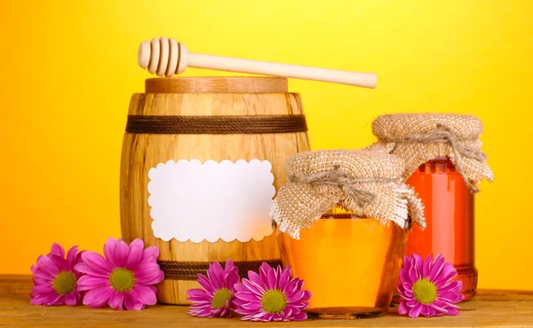 Zoete honing in potten en vat met drizzler op houten tafel op gele achtergrond — Stockfoto