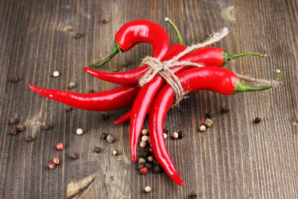 Red hot chili peppers tied with rope on wooden background — Stock Photo, Image