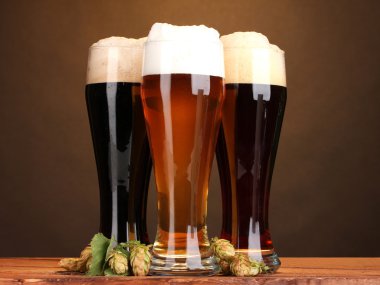 Three glasses with different beers and hop on wooden table on brown background