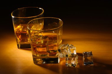 Two glasses of scotch whiskey and ice on wooden table clipart